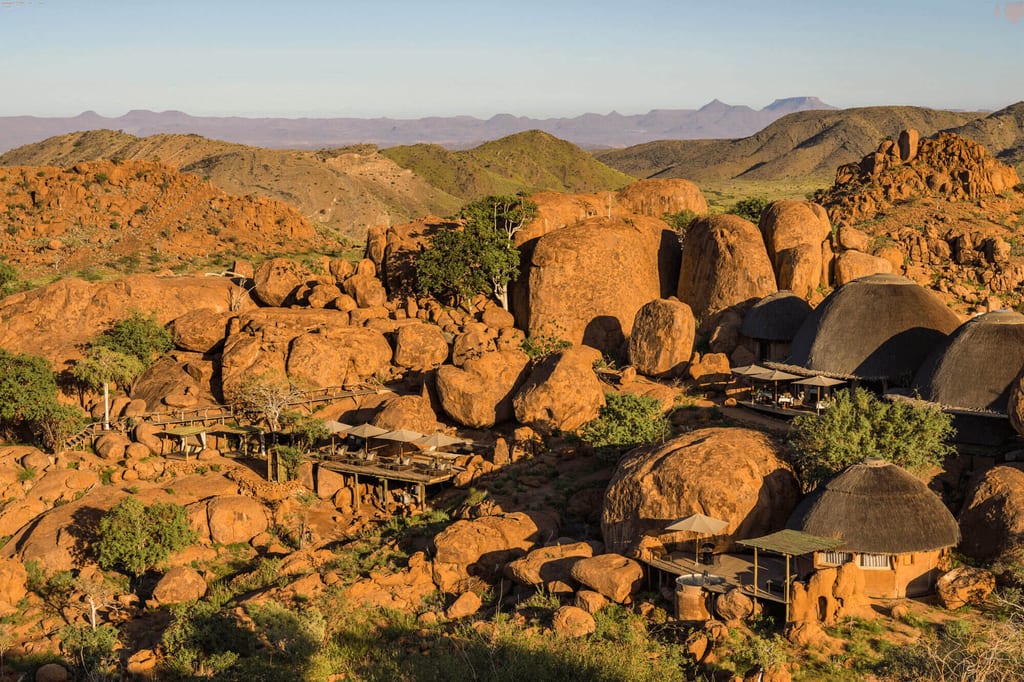 Felsige Landschaft mit runden Felsblöcken und strohgedeckten Lodges im warmen Abendlicht