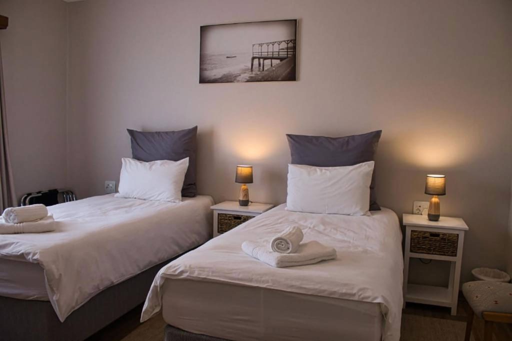 Zweibettzimmer mit weißen Bezügen, Nachttischen und warmen Tischlampen.