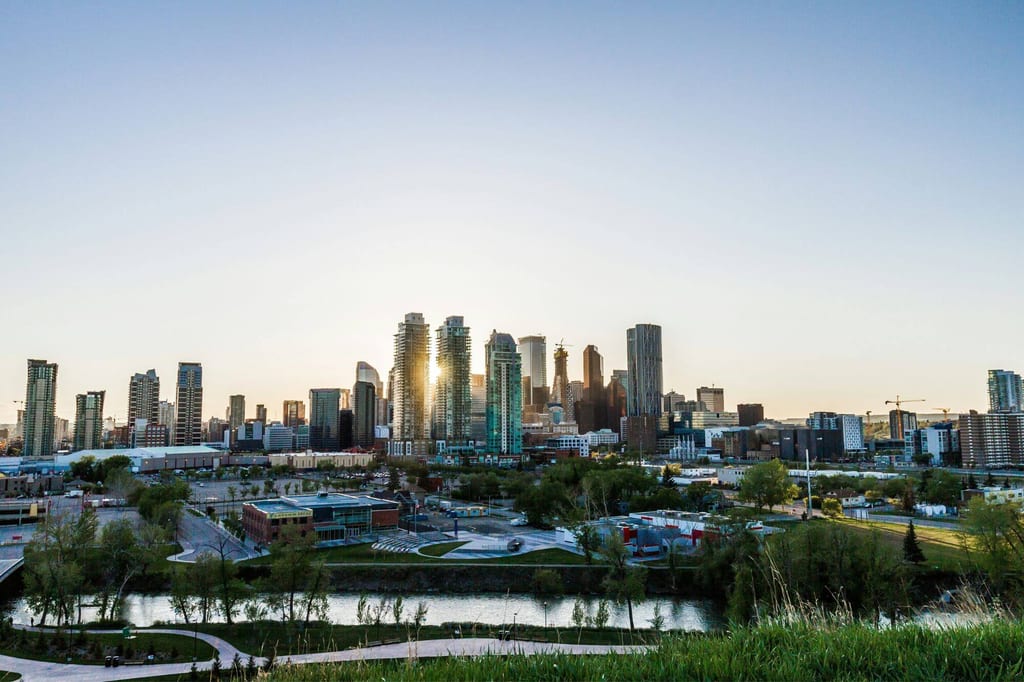 Panoramablick auf Calgary-Skyline mit Fluss und Park im Vordergrund bei Abendlicht.
