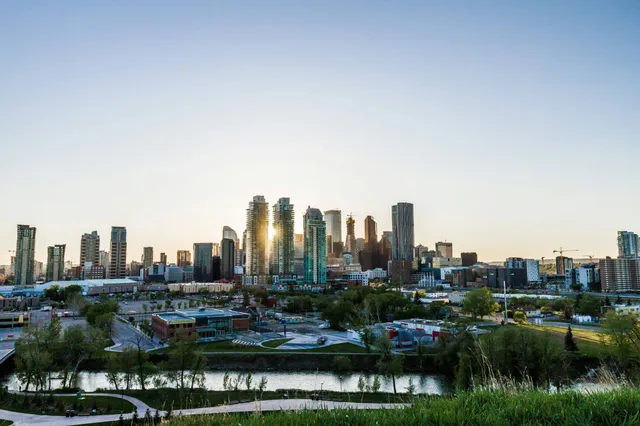 Panoramablick auf Calgary-Skyline mit Fluss und Park im Vordergrund bei Abendlicht.