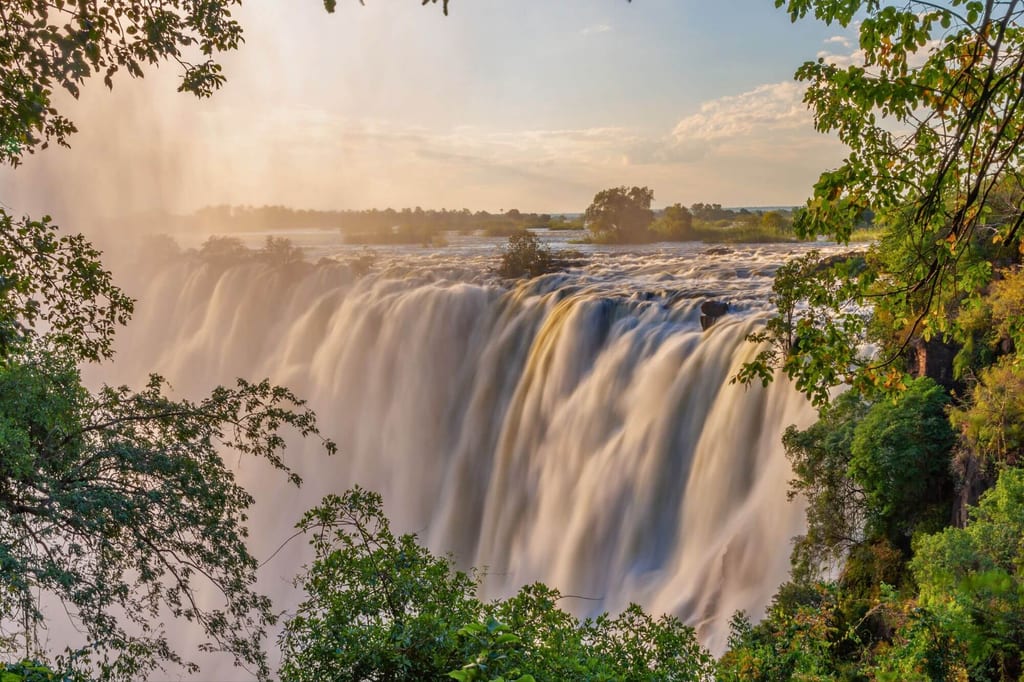 Großer Wasserfall in warmem Abendlicht, umrahmt von üppigen Bäumen und Dunst