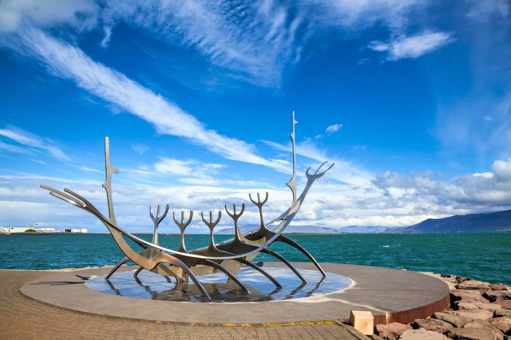 Silberne Boot-Skulptur auf runder Plattform am Meer bei blauem Himmel