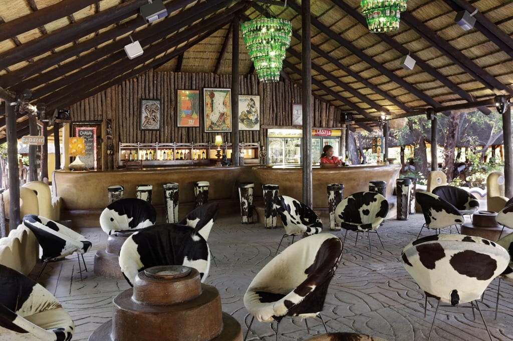 Offene Lodge-Bar mit Strohdach, runden schwarz-weißen Sesseln und langer Holztheke