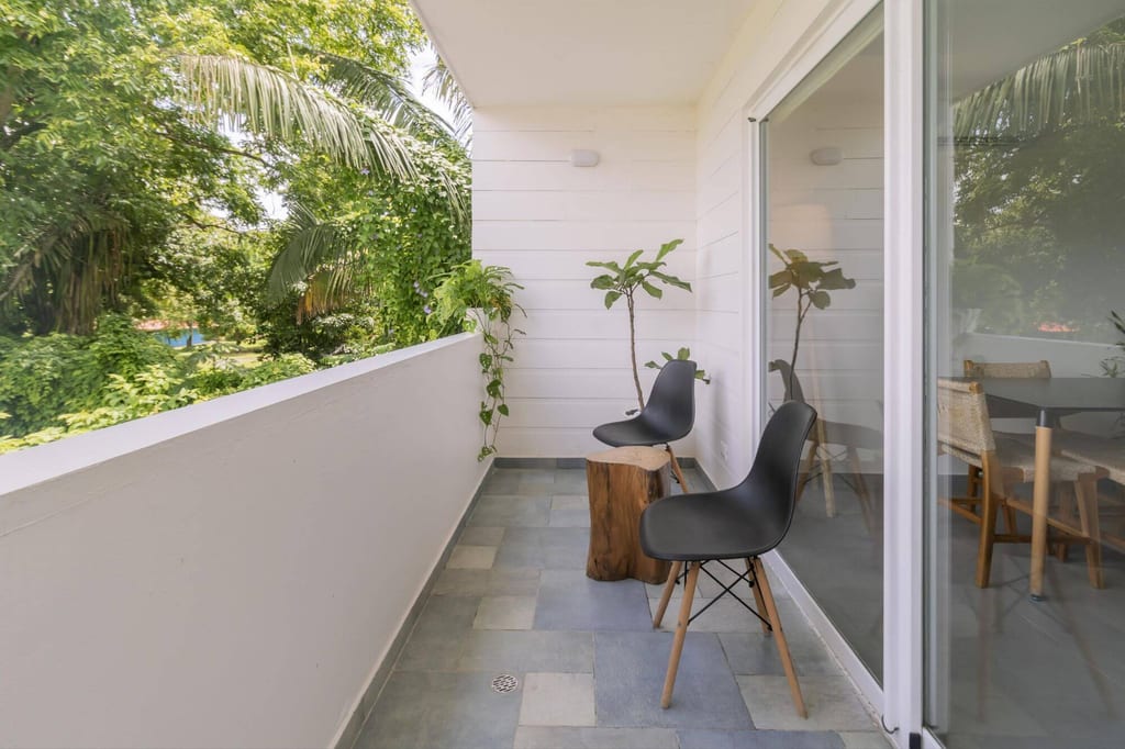 Heller Balkon mit zwei schwarzen Stühlen, Holzbeistelltisch und tropischem Grün im Hintergrund.