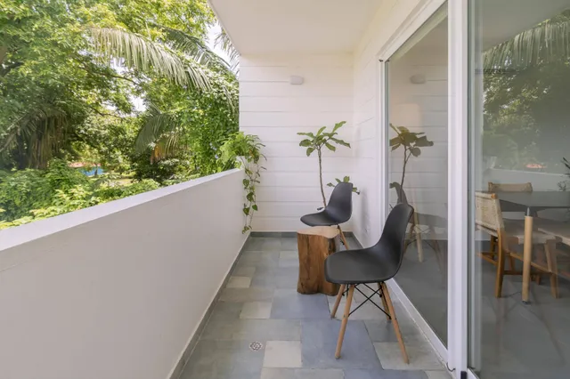 Heller Balkon mit zwei schwarzen Stühlen, Holzbeistelltisch und tropischem Grün im Hintergrund.
