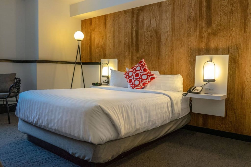 Gemütliches Hotelzimmer mit großem weißen Bett, Holz-Kopfteil und warmen Lampen.