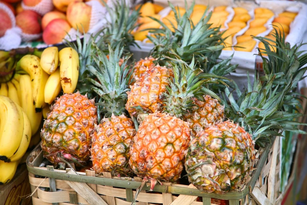 Mehrere Ananas in einem Holzkorb neben Bananen auf einem Marktstand, Nahaufnahme bei Tageslicht.