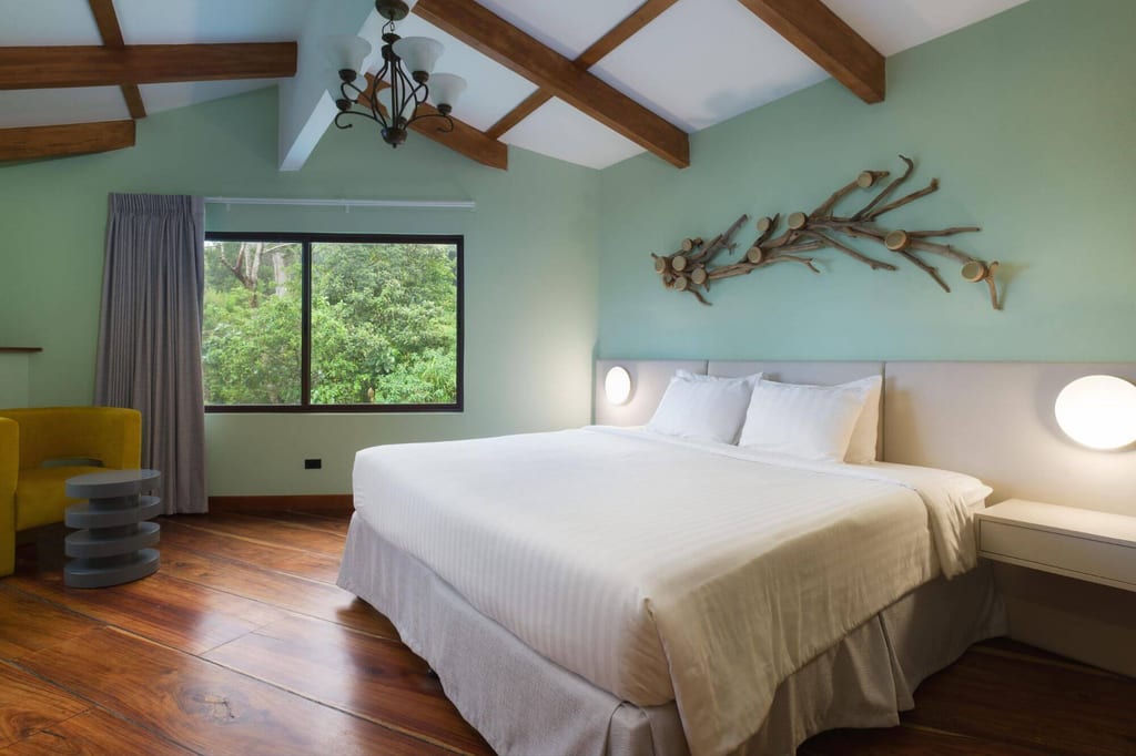 Helles Schlafzimmer mit Doppelbett, Fensterblick auf Bäume und Holzbalken an der Decke.