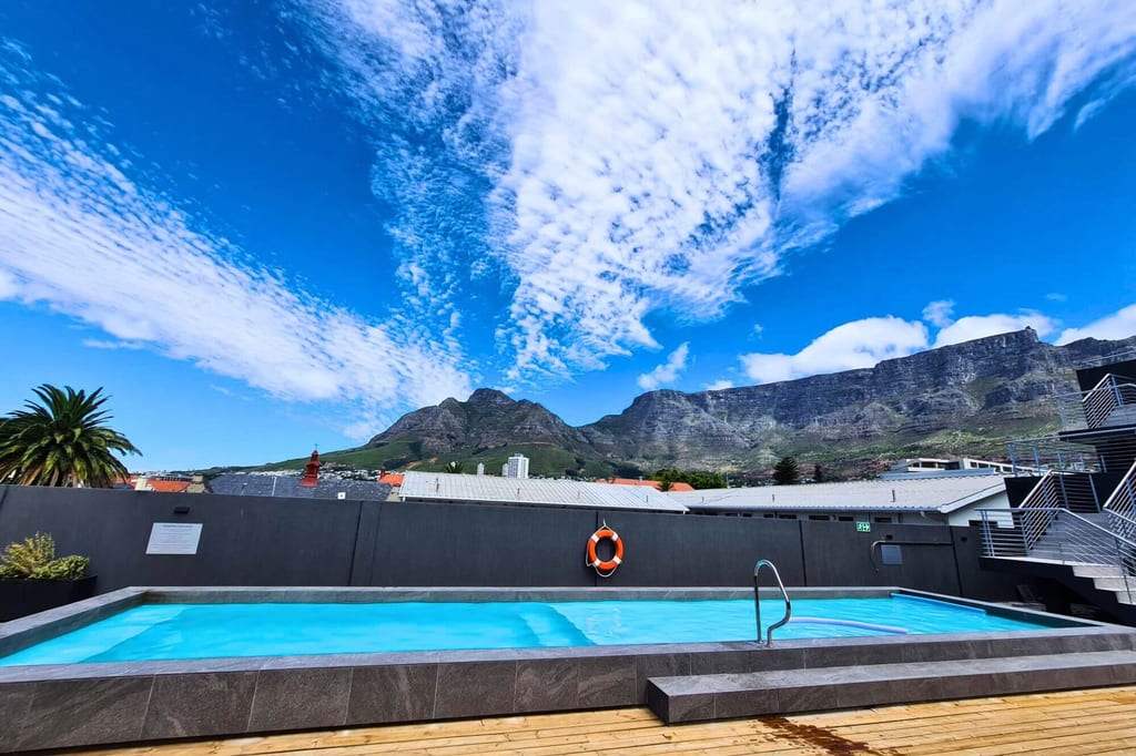 Dachterrassen-Pool vor einer steilen Bergkette unter blauem Himmel mit Schleierwolken.