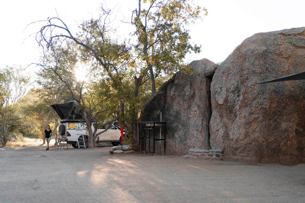 Campingfahrzeug mit Dachzelt neben großen Felsen bei warmem Spätnachmittagslicht, Person am Rand