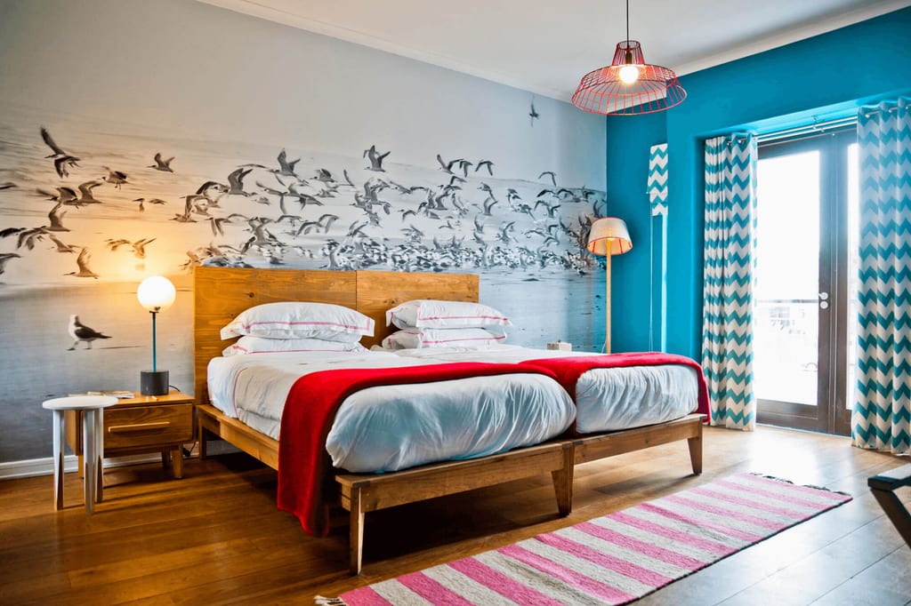 Modernes Doppelzimmer mit Holzbett, Wandgrafik fliegender Vögel und Tageslicht durch Glastür.