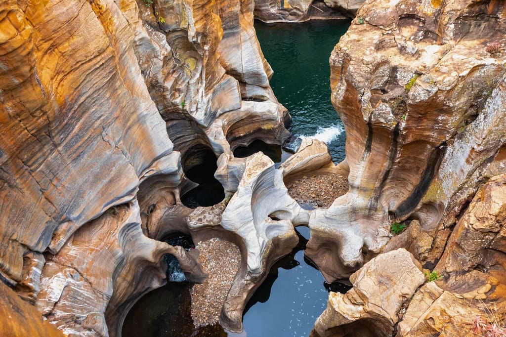 Blick von oben auf ausgerundete Felsbecken und dunkles Wasser in einem sandsteinernen Canyon.