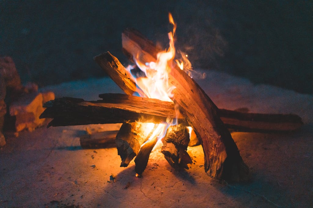 Nahaufnahme eines brennenden Lagerfeuers auf Sand bei Nacht mit warmen Flammenlicht.