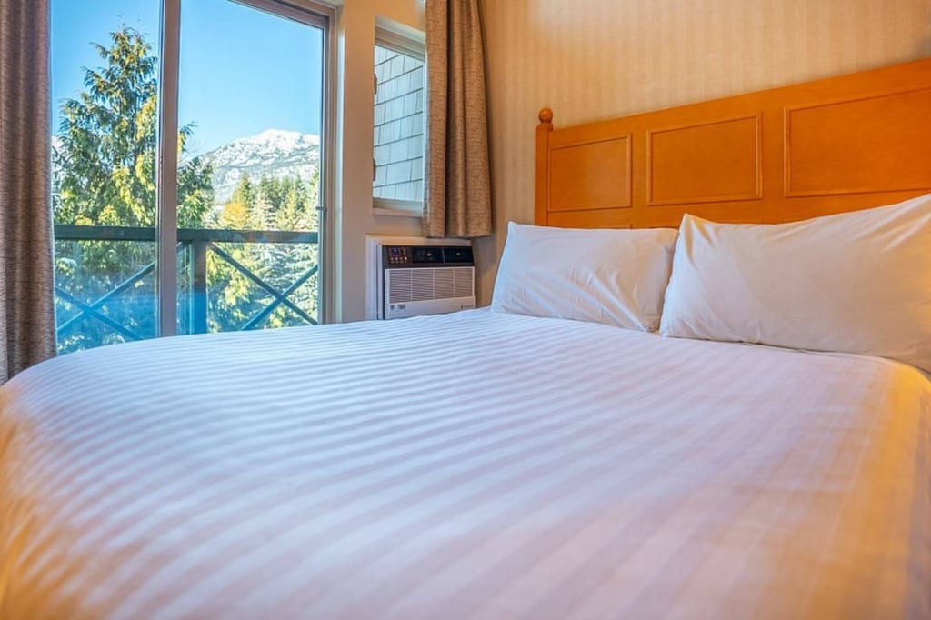 Blick über ein großes Bett in ein Zimmer mit Balkon und Bergblick bei klarem Tageslicht