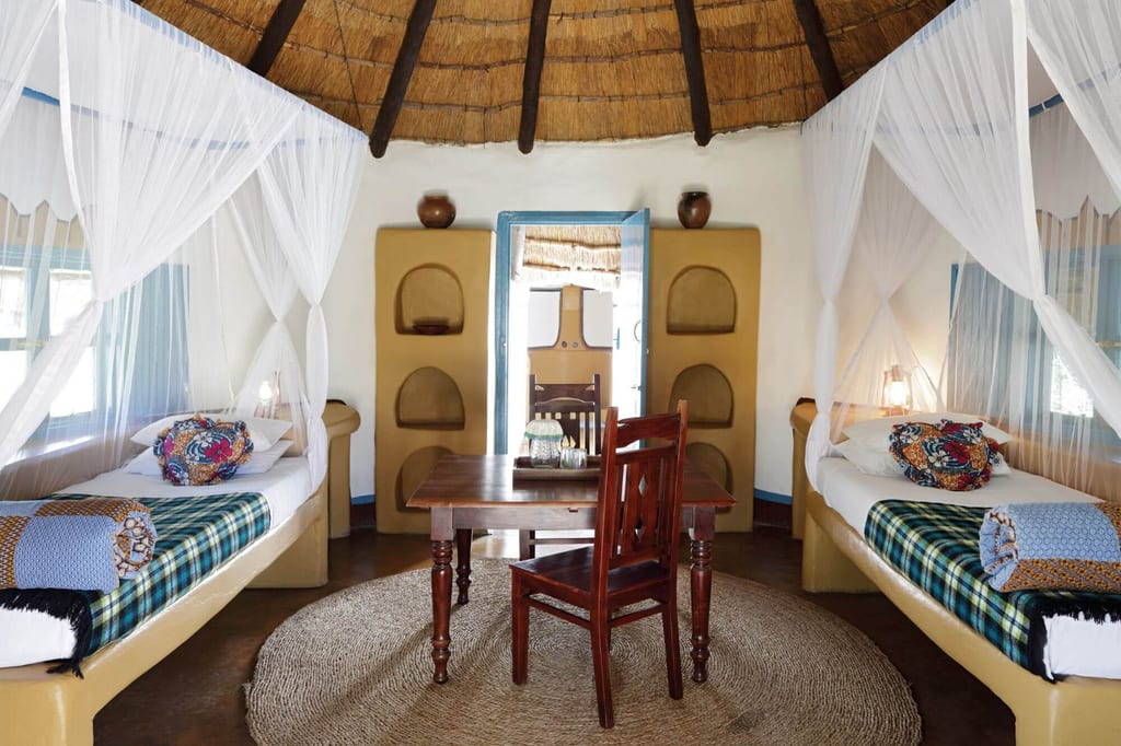 Rundes Lodgezimmer mit zwei Betten, Moskitonetzen und Holztisch in Tageslichtstimmung