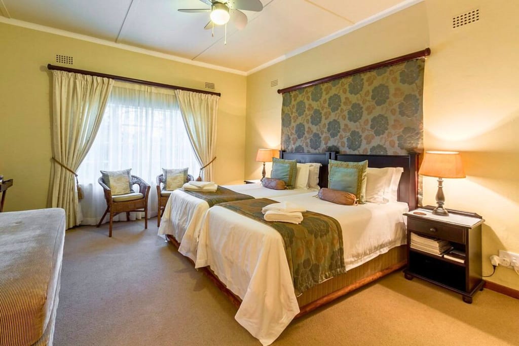 Gemütliches Gästezimmer mit zwei Einzelbetten, Sesseln am Fenster und warmer Beleuchtung.
