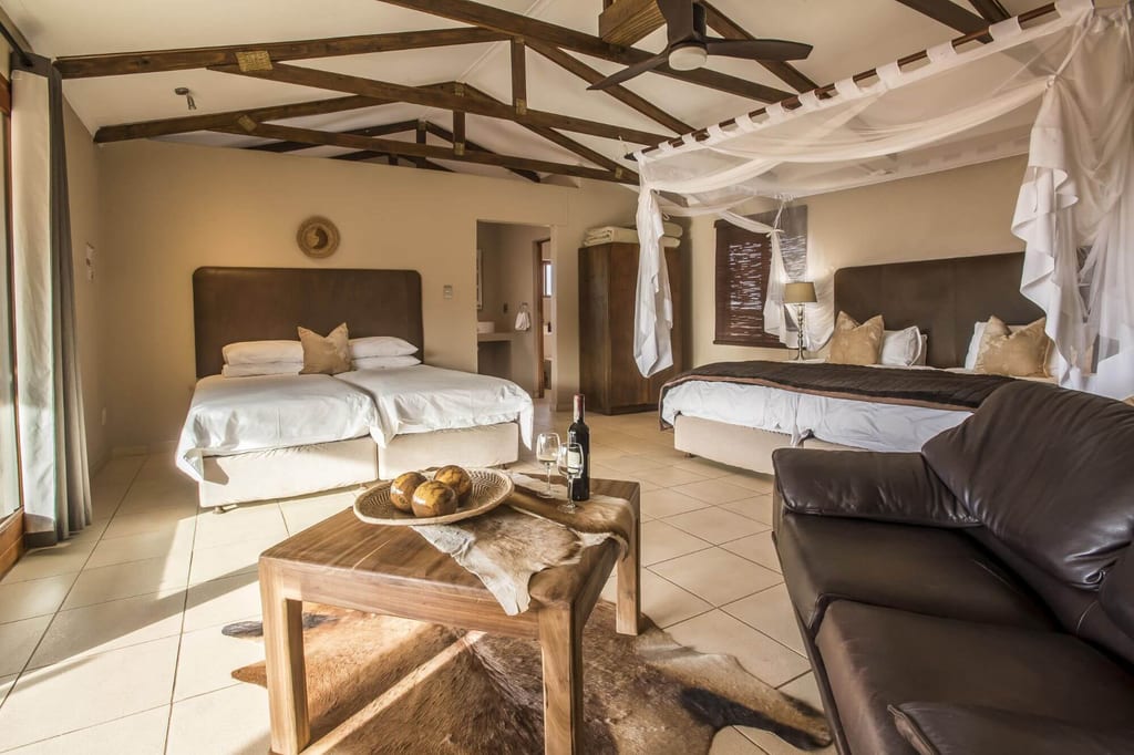 Helles Lodge-Zimmer mit zwei Betten, Baldachin, Ledersofa und Holztisch mit Weinflasche