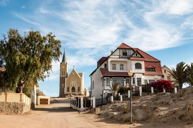 Straße in Lüderitz mit Kirche im Hintergrund und weißem Haus mit rotem Dach, sonniger Tag