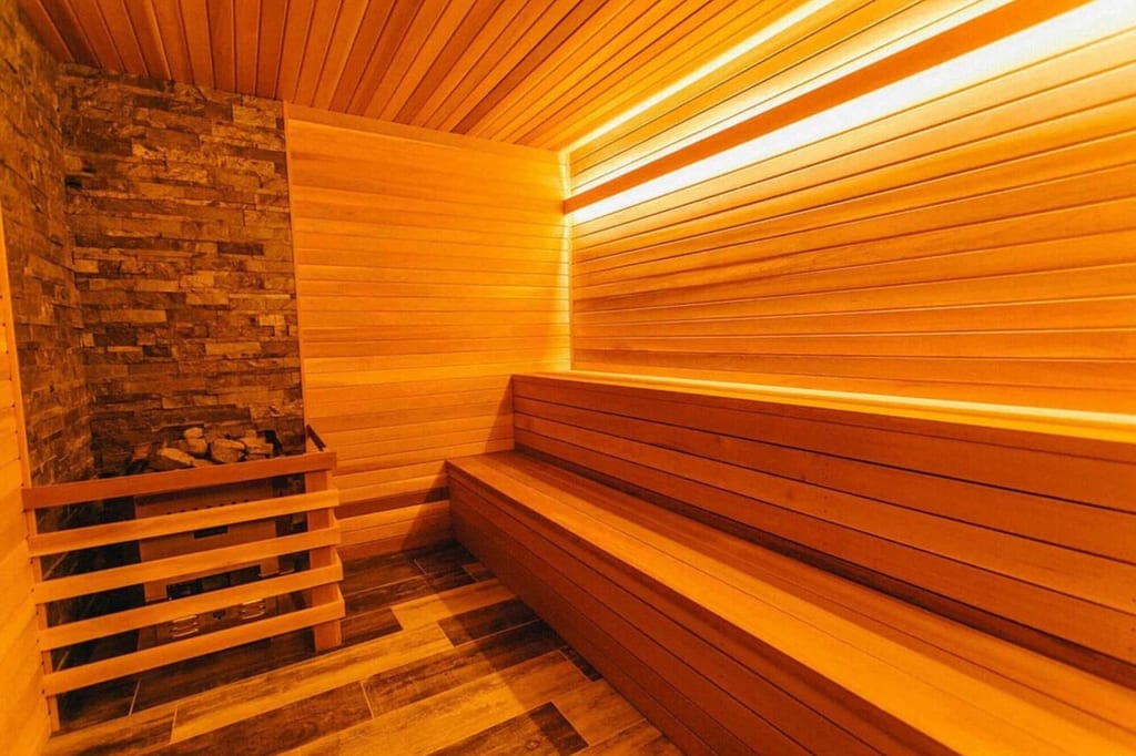 Innenansicht einer warm beleuchteten Holzsauna mit Sitzbänken und Saunaofen