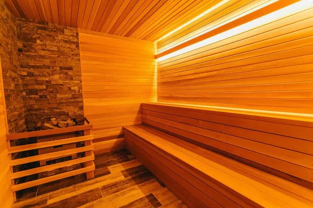 Innenansicht einer warm beleuchteten Holzsauna mit Sitzbänken und Saunaofen