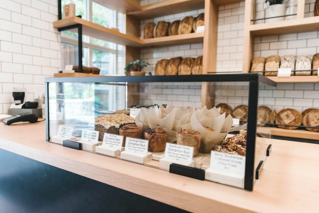 Glastheke mit verschiedenen Gebäckstücken vor Regalen mit Brot in einer hellen Bäckerei