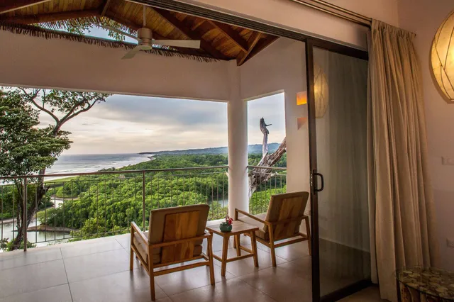 Balkon mit zwei Holzstühlen und Meerblick über grüne Küstenlandschaft bei gedämpftem Licht.
