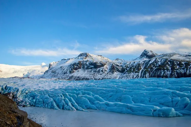 Blauer Gletscher im Vordergrund vor schneebedeckten Bergen bei klarem Tageslicht.