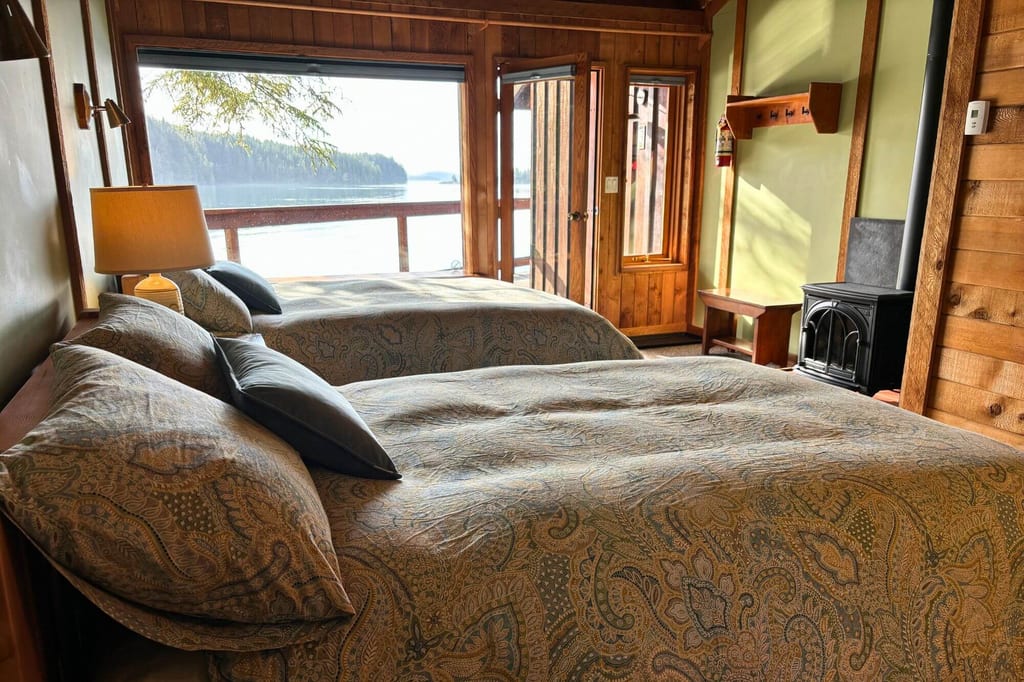 Gemütliches Holzschlafzimmer mit zwei Betten und Seeansicht durch große Fenster.