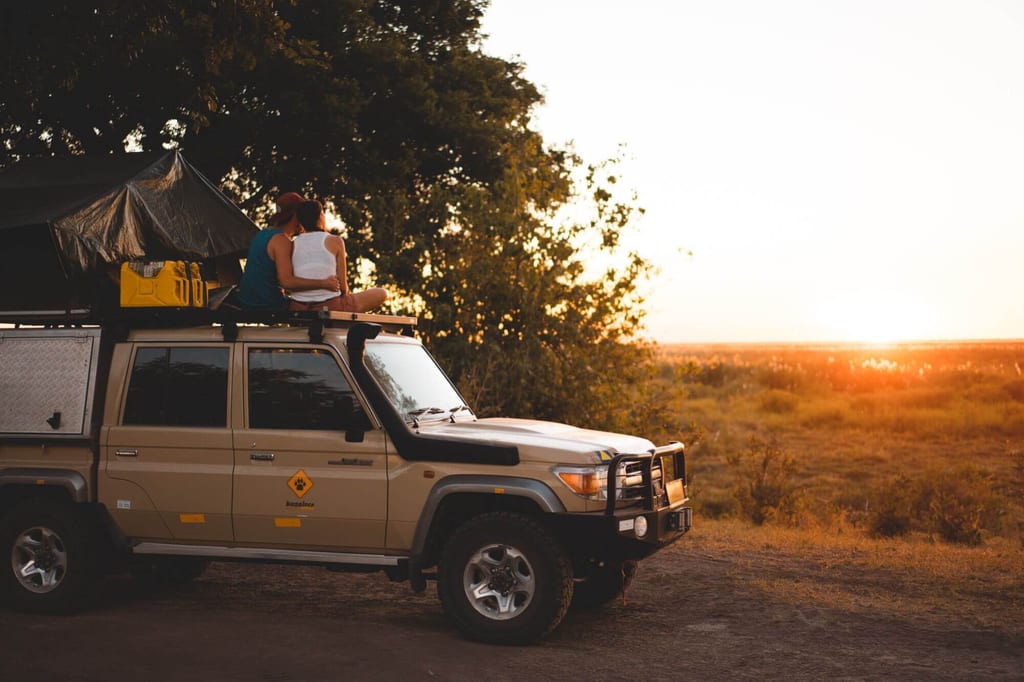 Paar sitzt auf dem Dach eines Safari-Geländewagens bei Sonnenuntergang in der Linyanti-Region, Botswana.