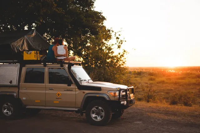 Paar sitzt auf dem Dach eines Safari-Geländewagens bei Sonnenuntergang in der Linyanti-Region, Botswana.