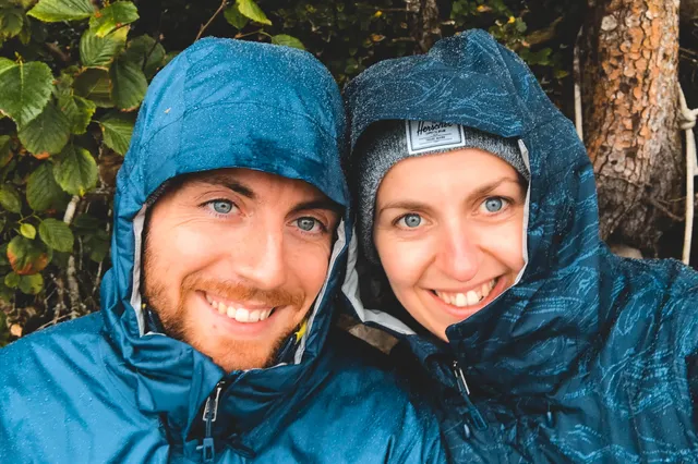 Nahaufnahme zweier lächelnder Personen in Kapuzenjacken bei Regen im Wald