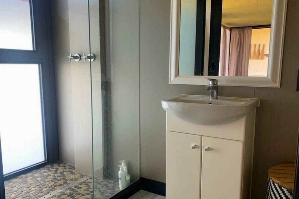 Badezimmer mit Waschbecken, Spiegel und Glasdusche mit kieselsteinboden, Tageslicht durch frostfenster