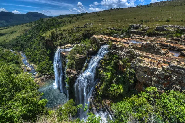 Mehrstämmiger Wasserfall von felsiger Hochfläche in grünes Tal bei hellem Tageslicht