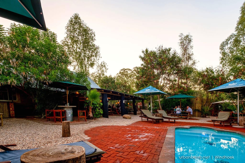 Gemütliche Lodge-Terrasse mit Pool, Liegen und Sonnenschirmen im warmen Abendlicht.