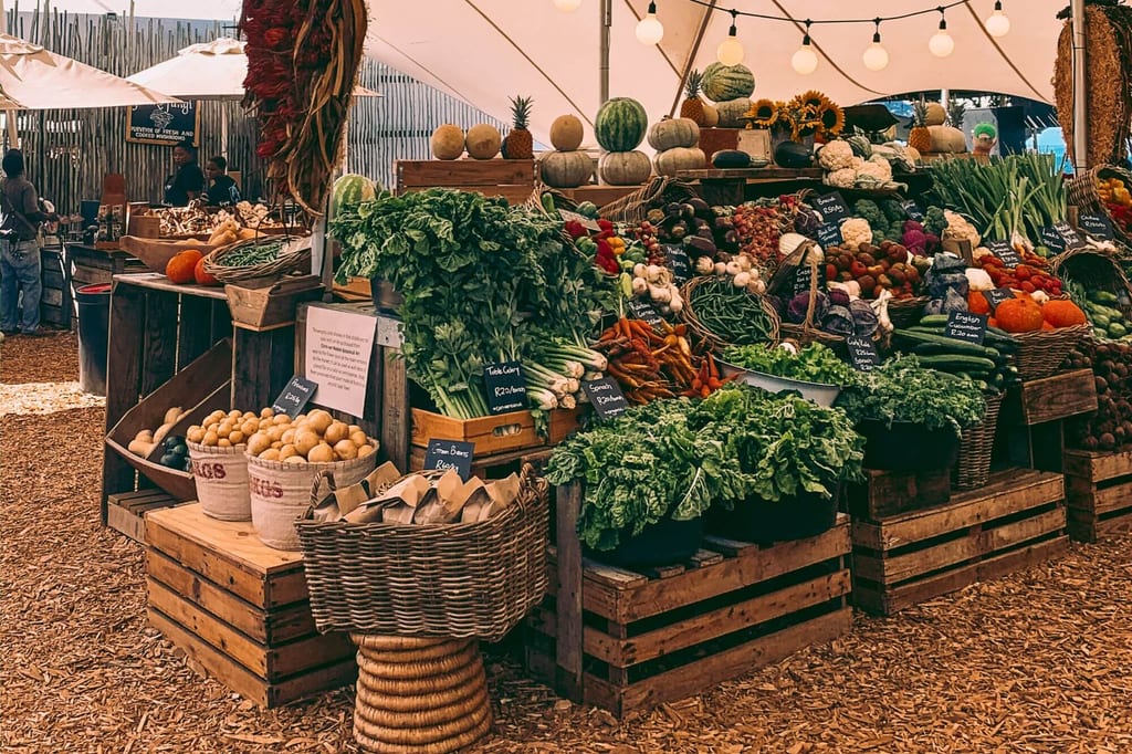 Marktstand mit Holzkisten und Körben voller Gemüse und Obst unter einem Zelt