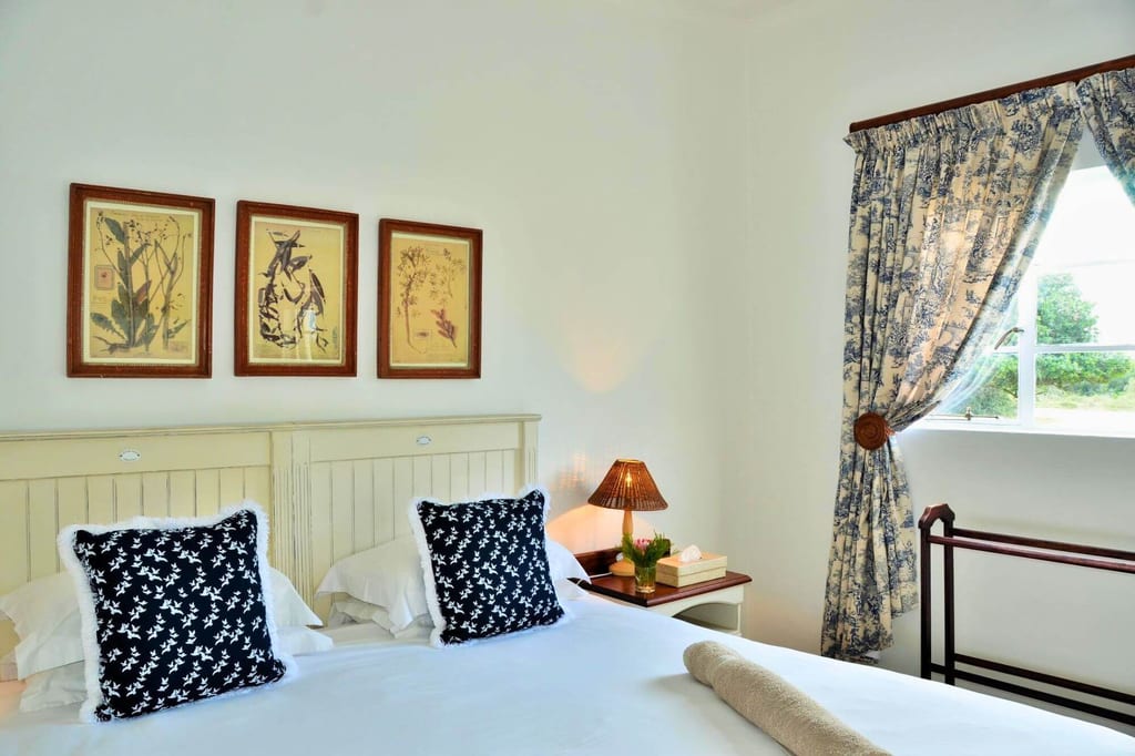 Helles Schlafzimmer mit Doppelbett, zwei gemusterten Kissen und Fenster mit floralen Vorhängen.