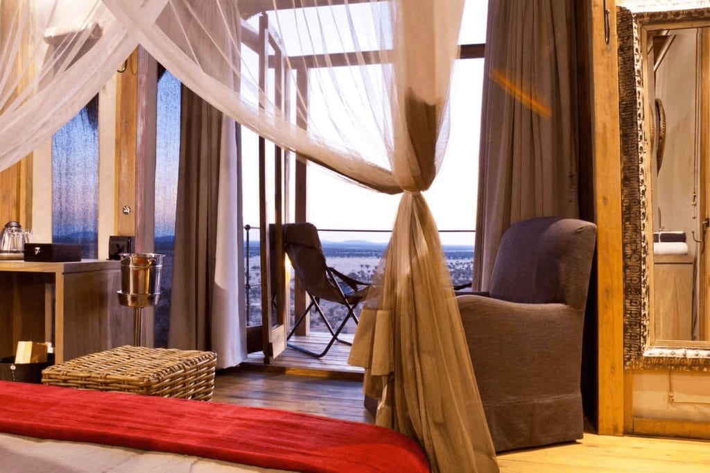 Gemütliches Lodge-Schlafzimmer mit Himmelbett, Moskitonetz und offenem Balkon zum Abendblick.