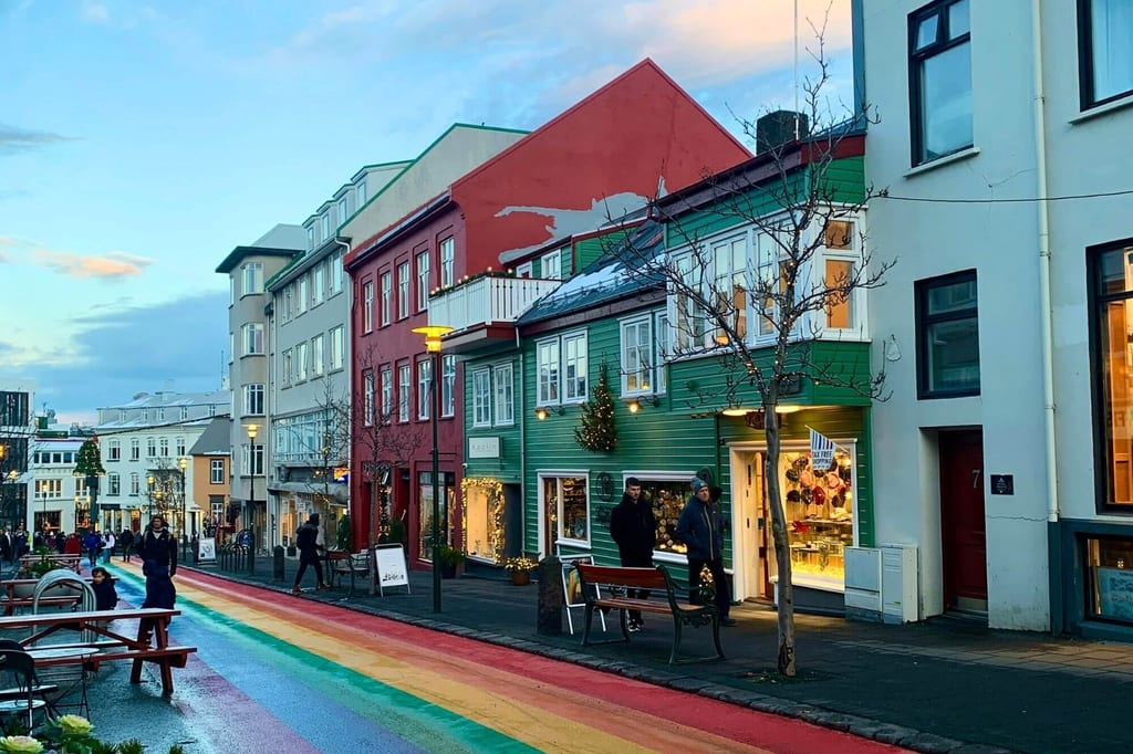 Straßenszene in Reykjavík mit bunten Häusern und einem regenbogenfarbenen Fußgängerweg bei Dämmerung.