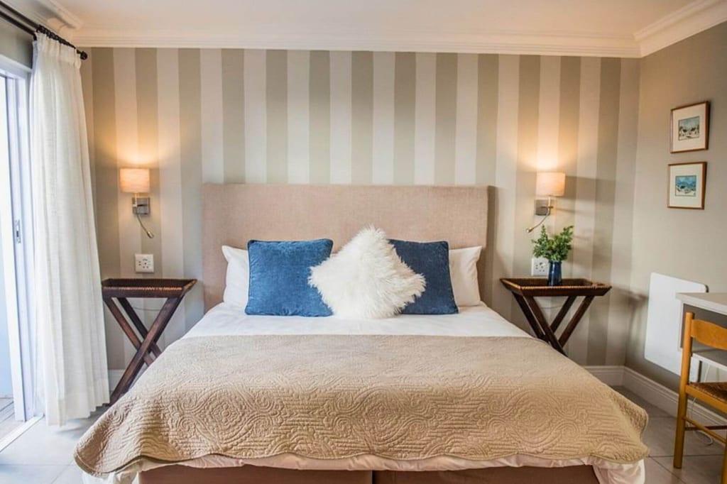 Frontale Aufnahme eines gemütlichen Schlafzimmers mit Doppelbett, blauen Kissen und gestreifter Wand.
