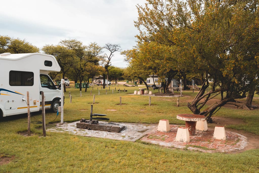 Wohnmobile auf einem grasigen Campingplatz mit Picknicktisch und Grillstelle bei bewölktem Himmel.
