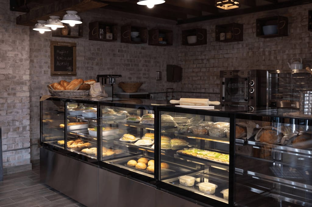 Bäckereiinnere mit beleuchteter Glasvitrine voller Brot und Gebäck vor Ziegelwand.
