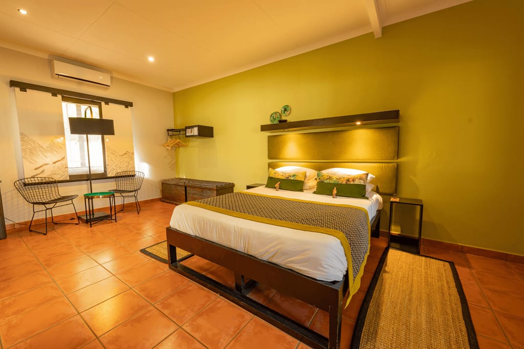 Modernes Hotelzimmer mit Doppelbett, grüner Wand und Sitzbereich bei warmem Licht.