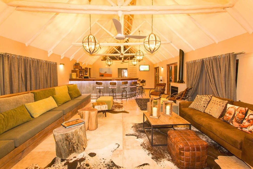 Weitwinkelaufnahme einer gemütlichen Lodge-Lounge mit Sofas, Bar und warmem Licht.