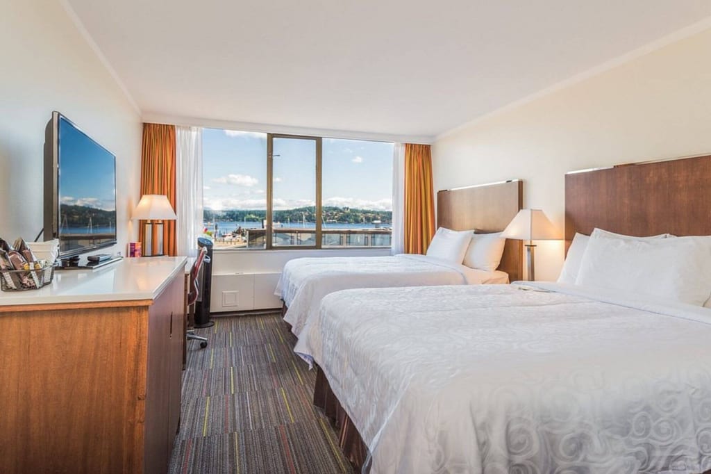 Helles Hotelzimmer mit zwei Doppelbetten und großem Fenster mit Blick aufs Wasser.