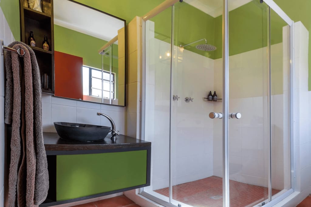 Helles Badezimmer mit Glasdusche, schwarzer Waschschale und grünen Wänden, seitliche Perspektive.
