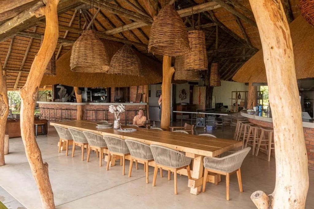 Offener Lodge-Innenraum mit langem Holztisch, geflochtenen Lampen und Reetdach