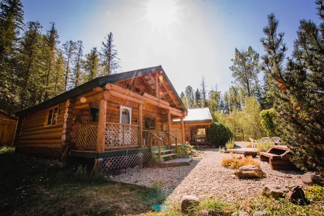 Rustikale Blockhütte mit Veranda in sonniger Waldlichtung und Kiesgarten