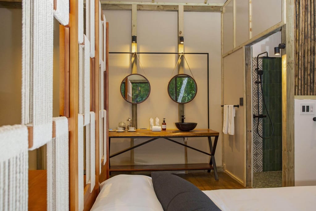 Innenansicht eines gemütlichen Lodge-Zimmers mit Waschtisch, zwei runden Spiegeln und offener Dusche.