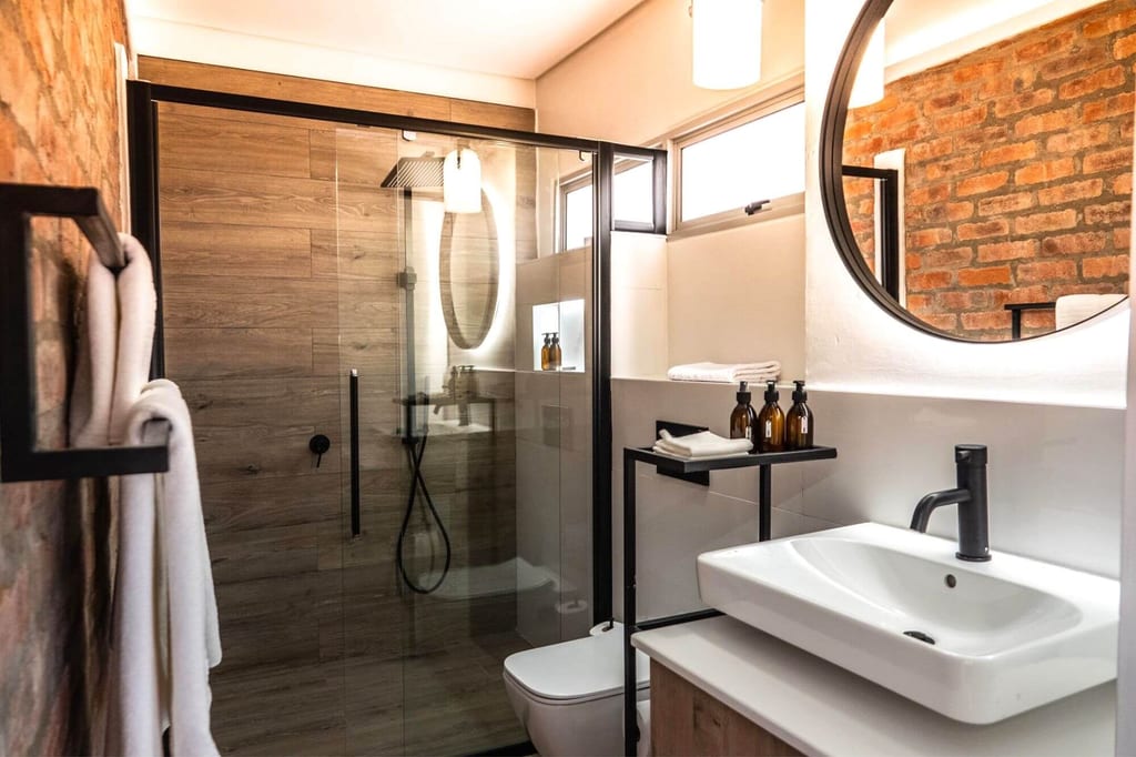 Modernes Badezimmer mit Glasdusche, rundem Spiegel und Ziegelwand, warm beleuchtet.