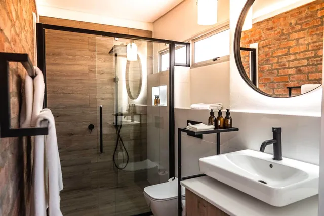 Modernes Badezimmer mit Glasdusche, rundem Spiegel und Ziegelwand, warm beleuchtet.